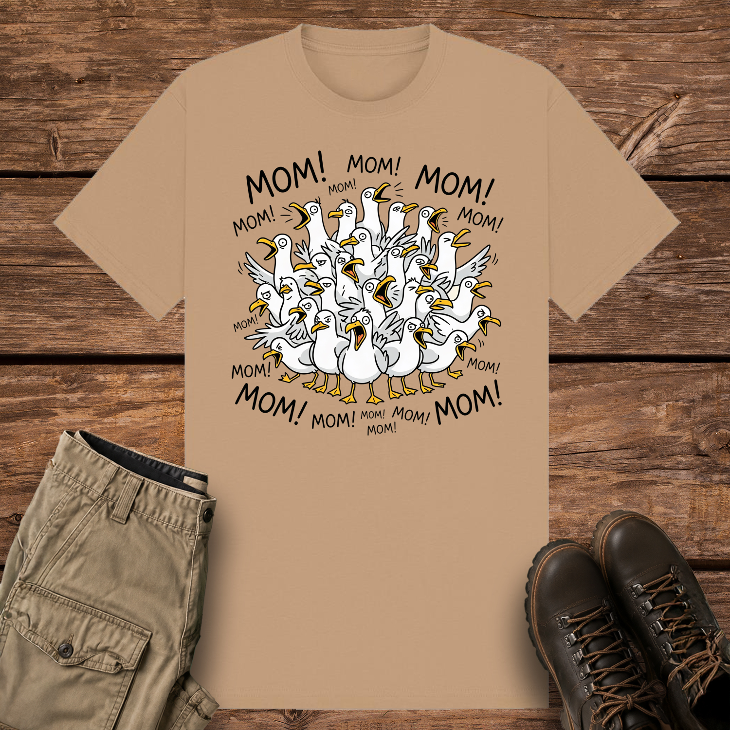 A camel-colored graphic t-shirt featuring a funny cartoon illustration of a crowded flock of squawking seagulls with their beaks wide open. The word "MOM!" is written repeatedly in a circle surrounding the frantic birds.