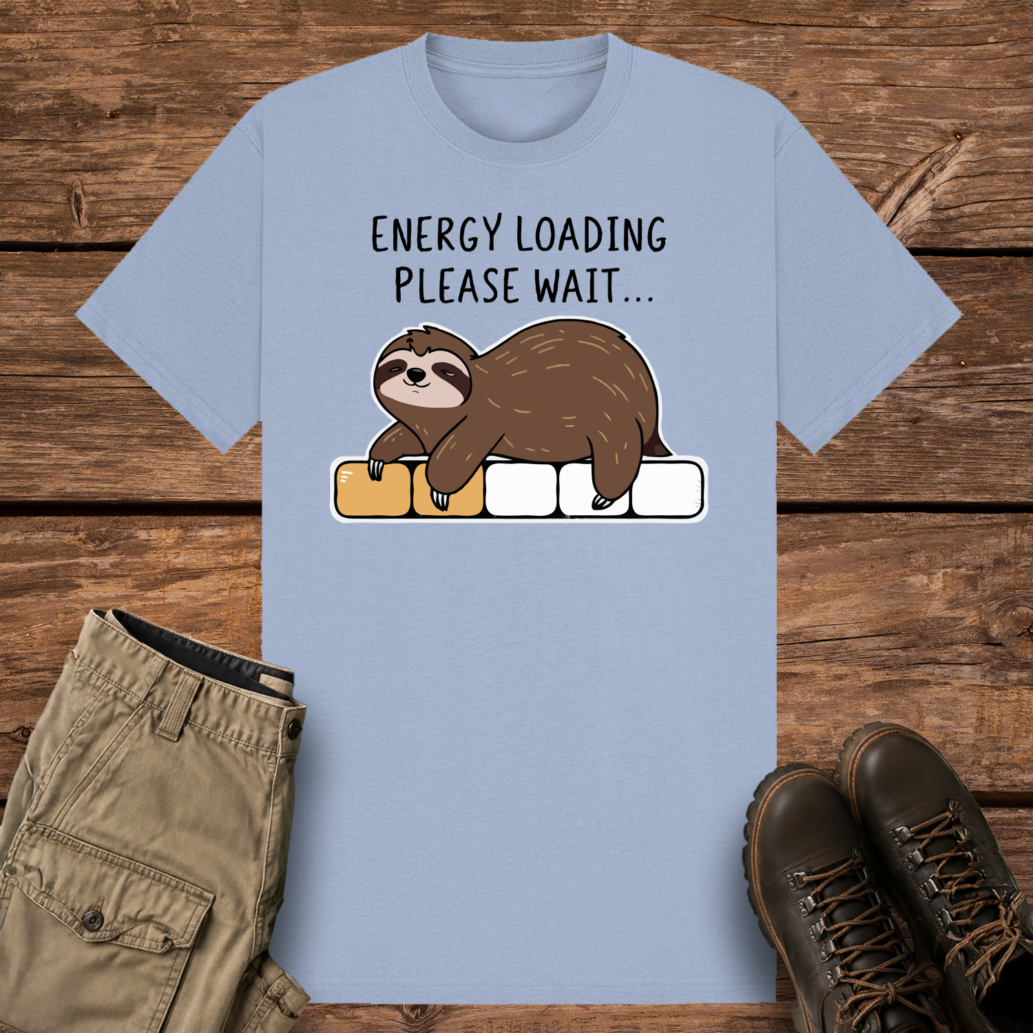 A pastel blue-colored graphic t-shirt featuring a cute cartoon illustration of a brown sloth lying face down on a progress loading bar that is only partially filled with yellow. Above the design, black text reads "ENERGY LOADING PLEASE WAIT..."