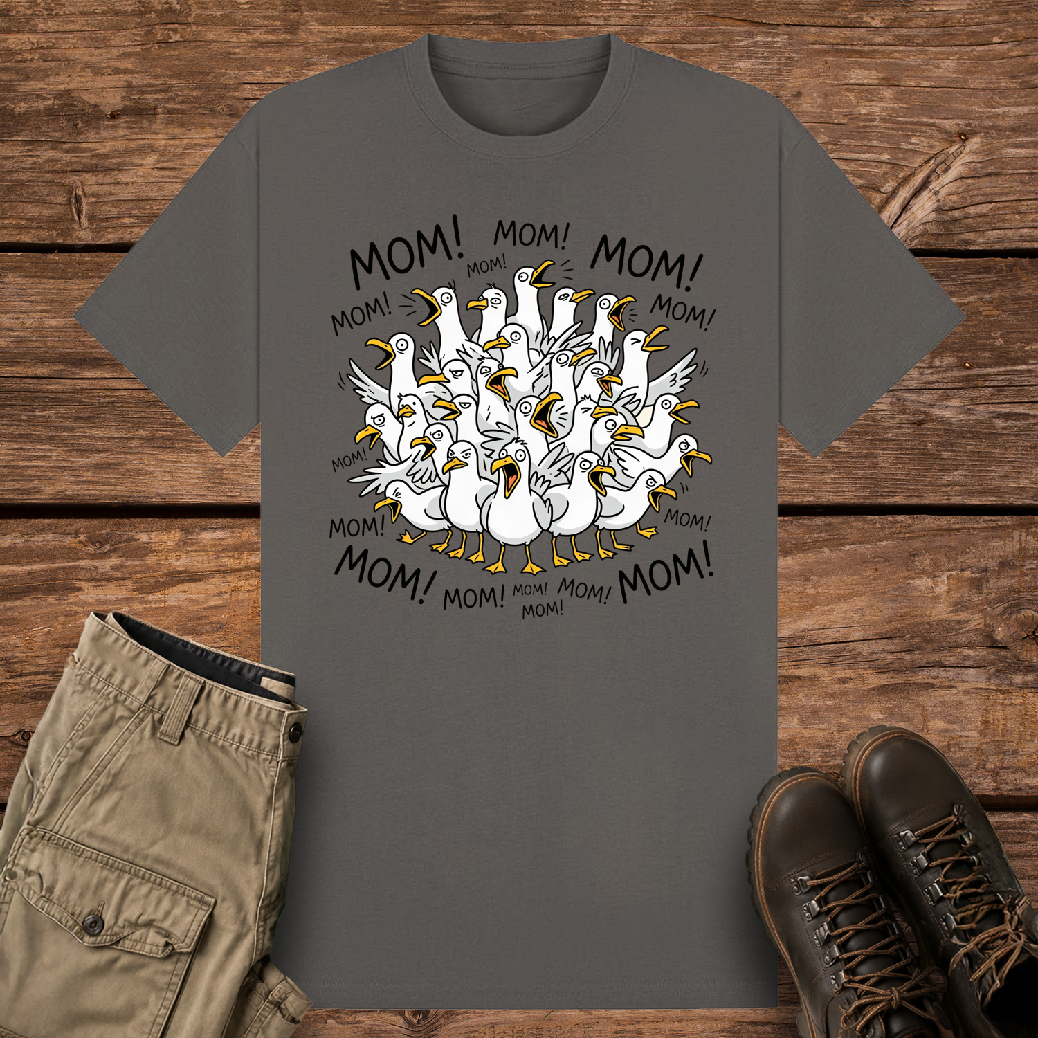A charcoal-colored graphic t-shirt featuring a funny cartoon illustration of a crowded flock of squawking seagulls with their beaks wide open. The word "MOM!" is written repeatedly in a circle surrounding the frantic birds.