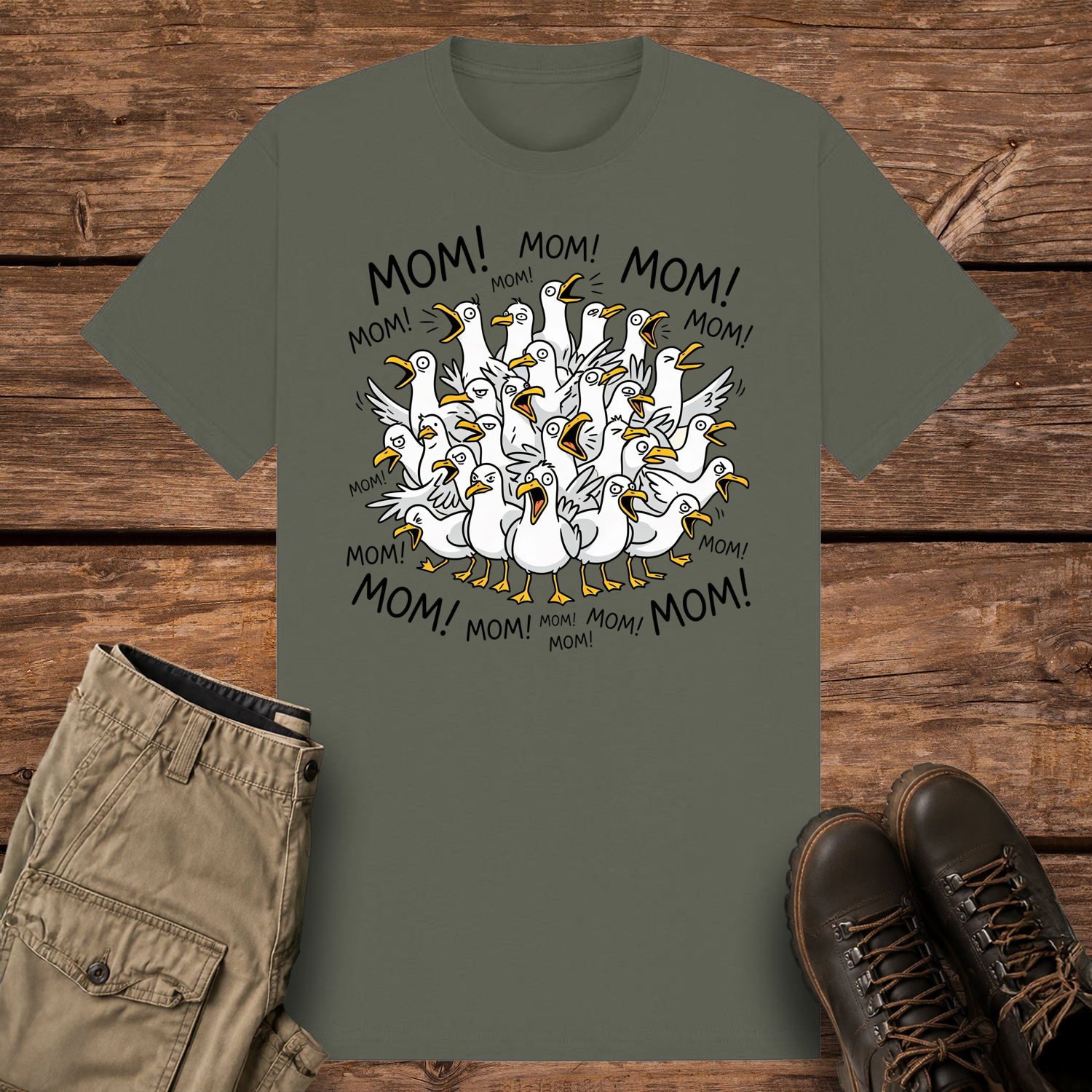 A khaki olive-colored graphic t-shirt featuring a funny cartoon illustration of a crowded flock of squawking seagulls with their beaks wide open. The word "MOM!" is written repeatedly in a circle surrounding the frantic birds.